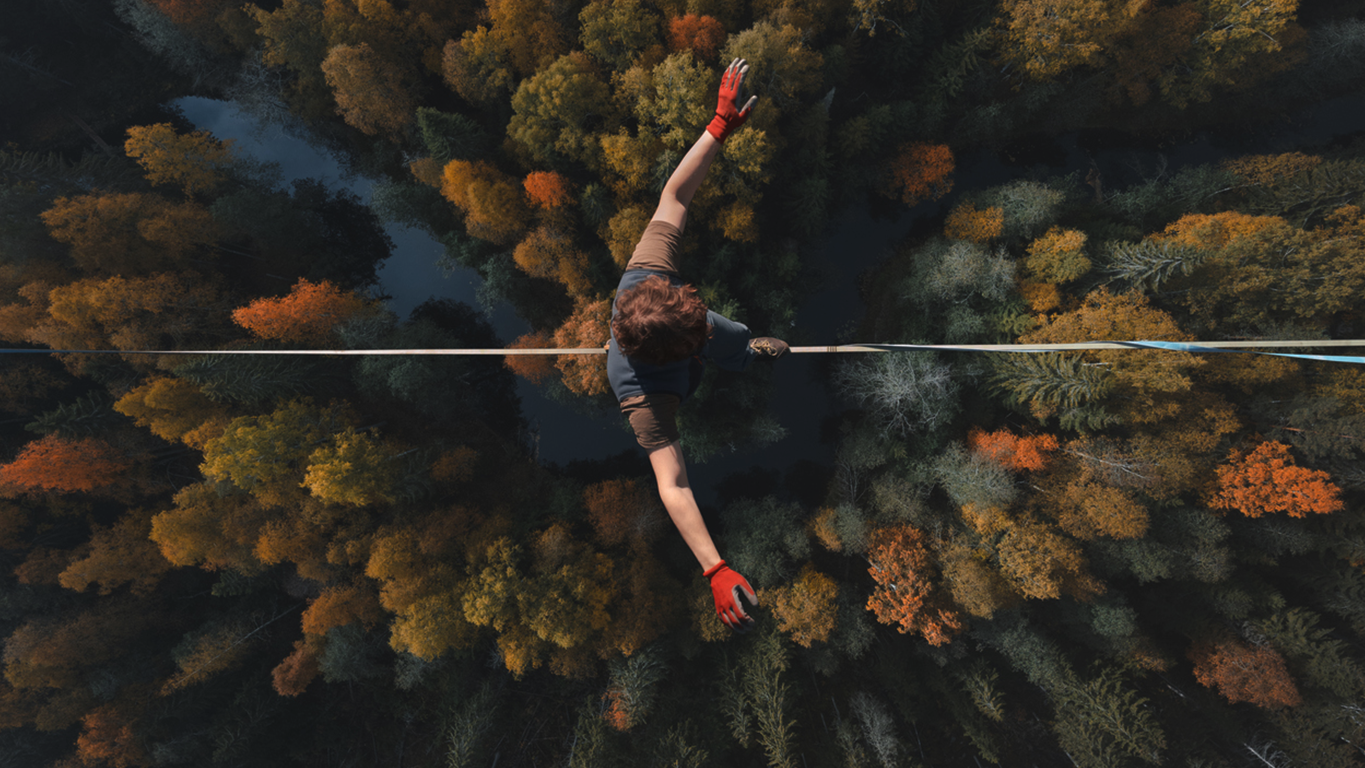 person balancing on a tightrope high above a forest, representing the precision of navigating vulnerability management.